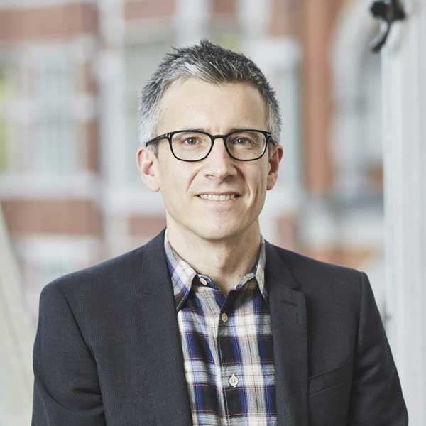 A photo of Trustee Cameron looking to camera. He is a white middle aged man with with white and grey hair wearing a dark blazer.